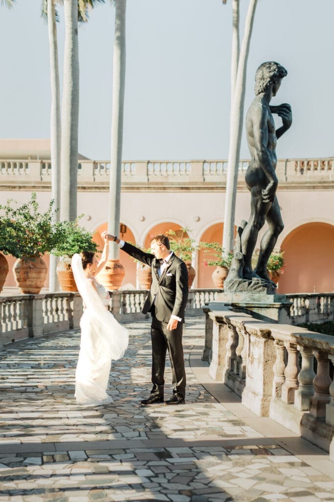 Bride twirling under groom’s arm in The Ringling Museum courtyard in Sarasota with statue and palm-lined architecture
