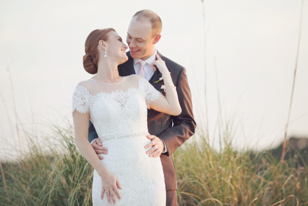 Bride and groom standing together at sunset near waterfront dunes
