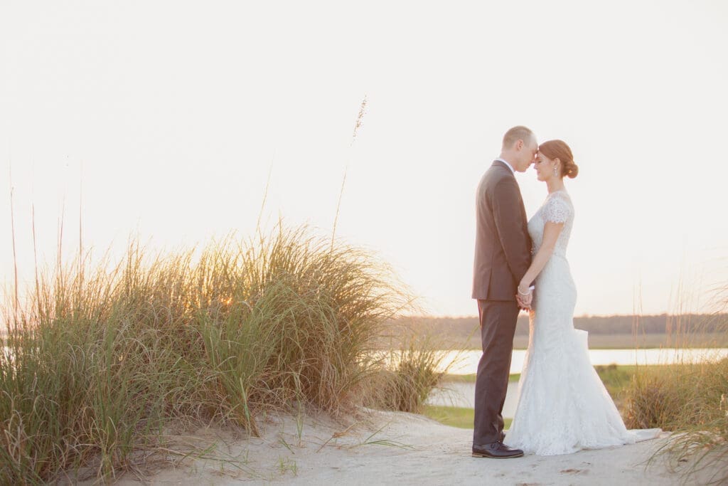 Bride and groom standing together at sunset near waterfront dunes